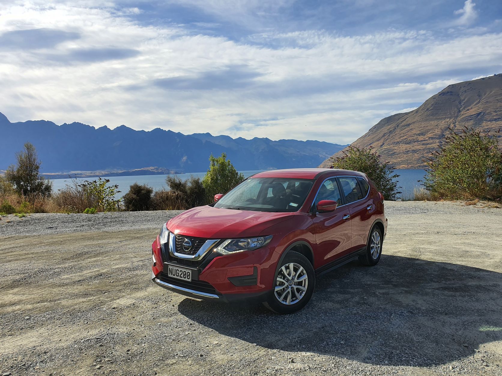 Red Nissan X-Trail with Queenstown Lake in the background