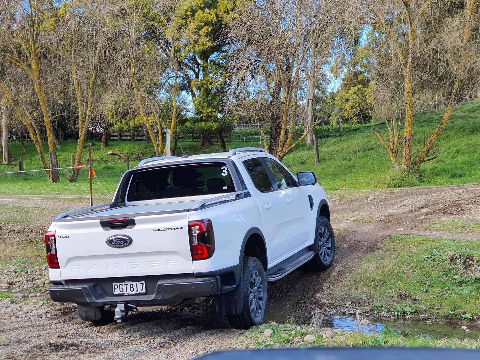A white 2022 Ford Ranger Wildtrak going off-road with one wheel suspended off the ground. Photo taken in Havelock North, New Zealand