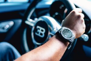 Photo of a man wearing a Bugatti smartwatch while driving a Bugatti hypercar
