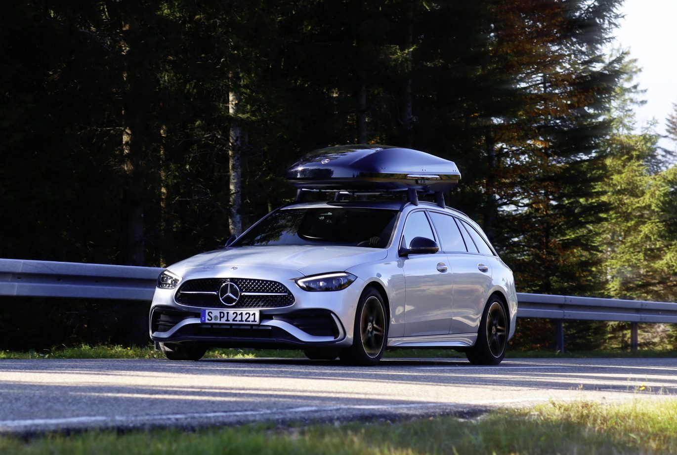 A zoomed out photograph of a Mercedes-Benz C-Class estate with a Mercedes-Benz roof box on top.