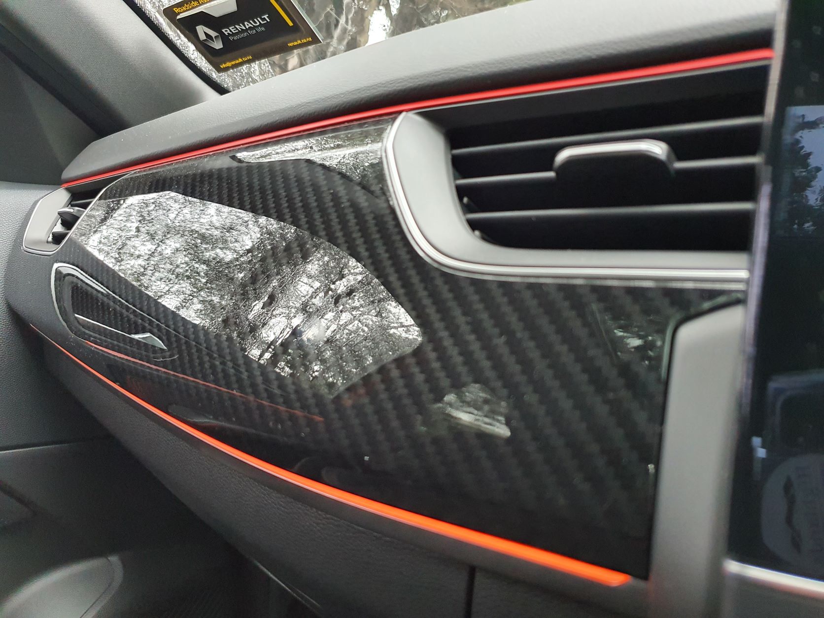 Faux carbon fibre trim on the dashboard of the Renault Arkana R.S Line highlighted in orange LEDs.