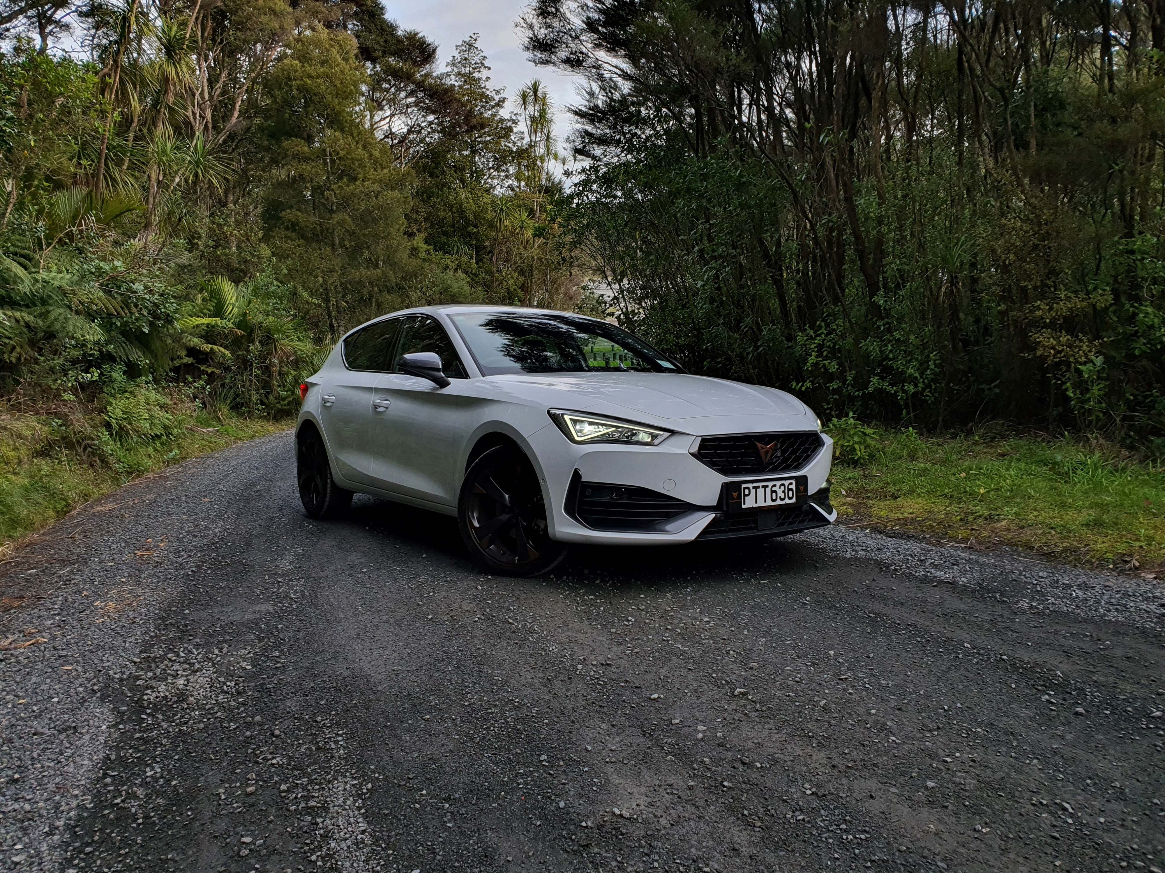 Front three quarters view of the 2023 Cupra Leon V in Nevada White with a green forest background