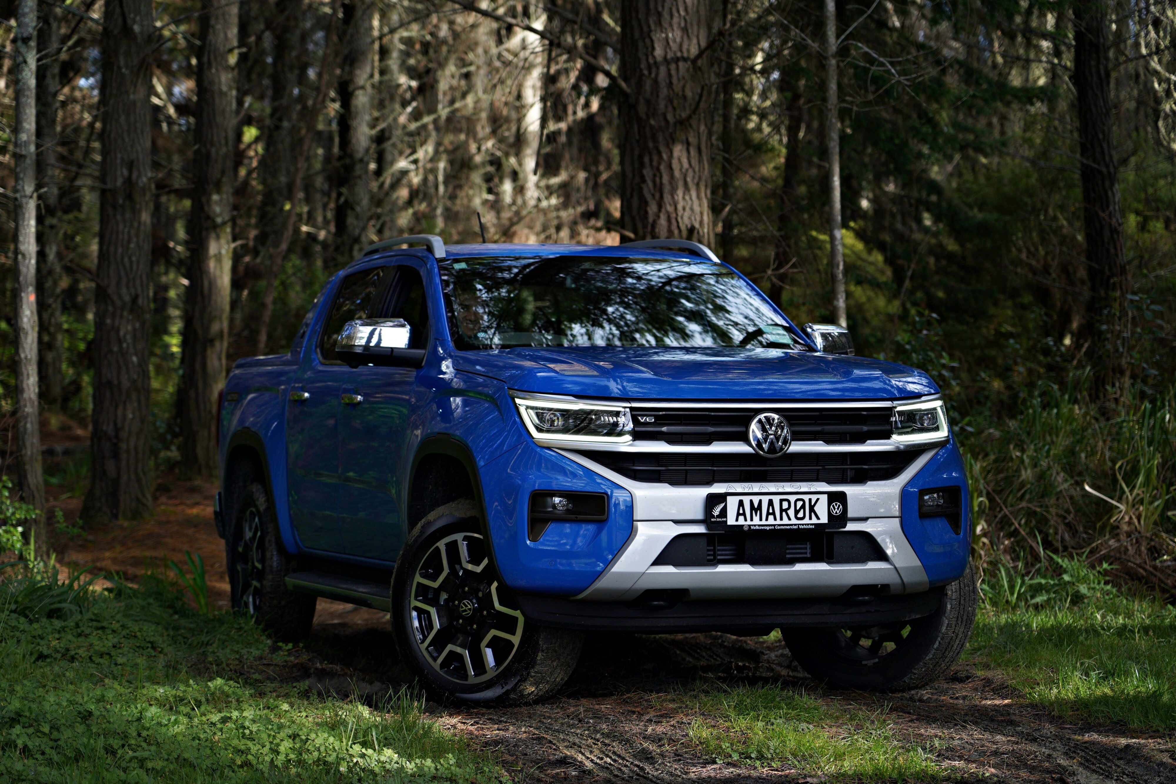 Front three quarters view of a blue Volkswagen Amarok Aventura in a forest.