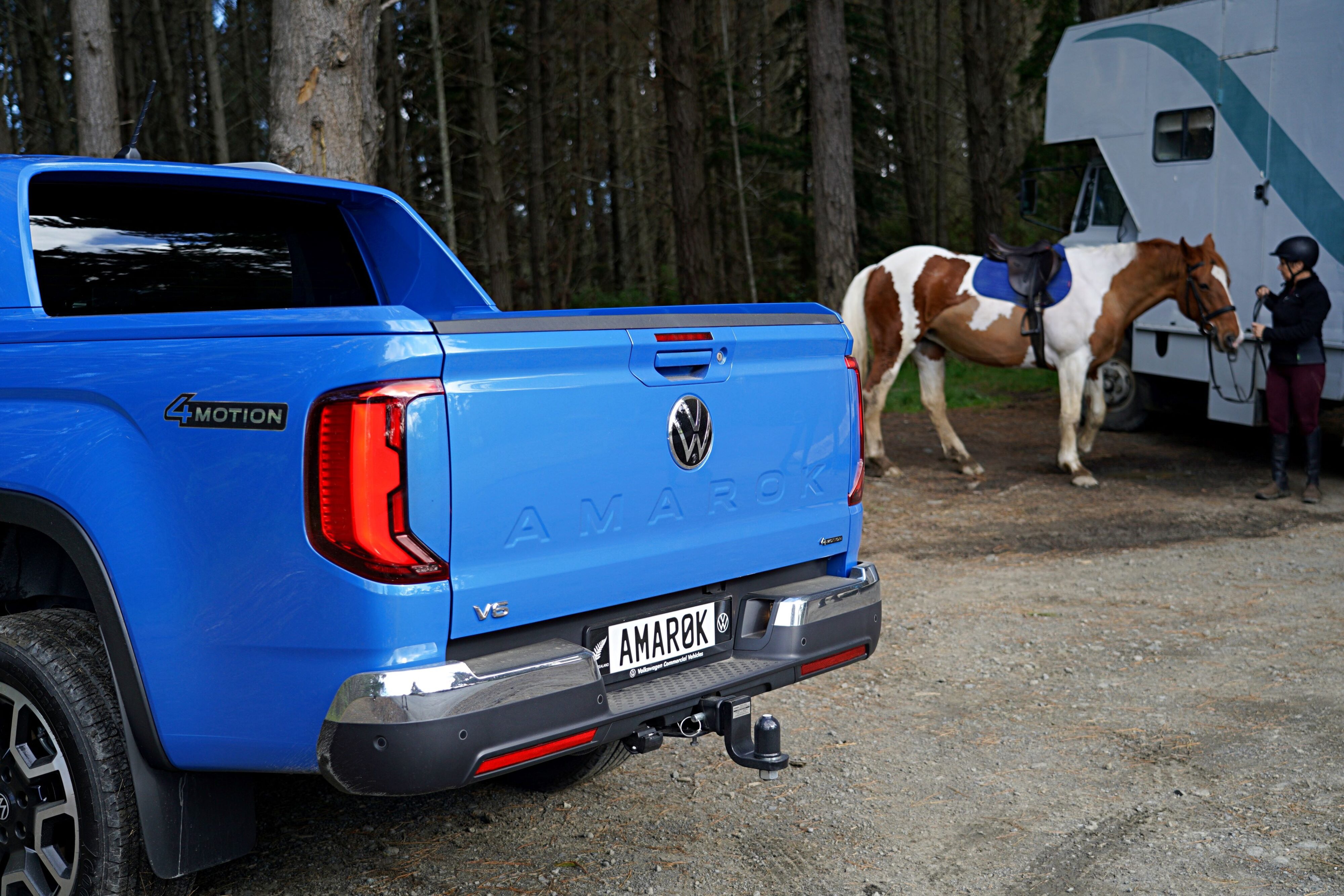 Rear of the 2023 Volkswagen Amarok Aventura in blue with a horse and horse float in the background