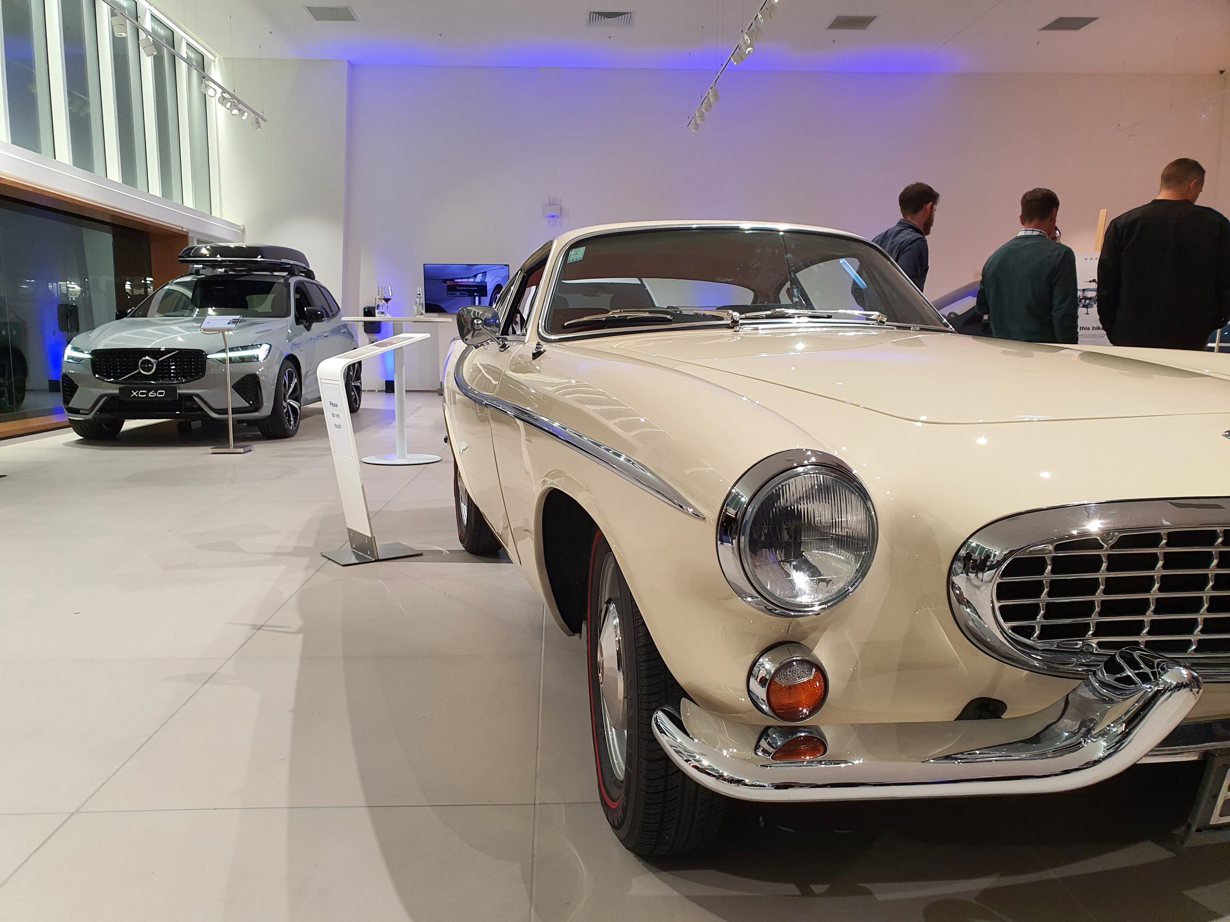 A white Volvo P1800S in the foreground with a grey Volvo XC60 in the background at the new Volvo NZ flagship store on Auckland's North Shore at Archibald & Shorter.