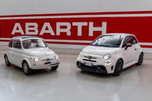 A photo of an old Abarth 595 parked next to a new Abarth 595, both in white.