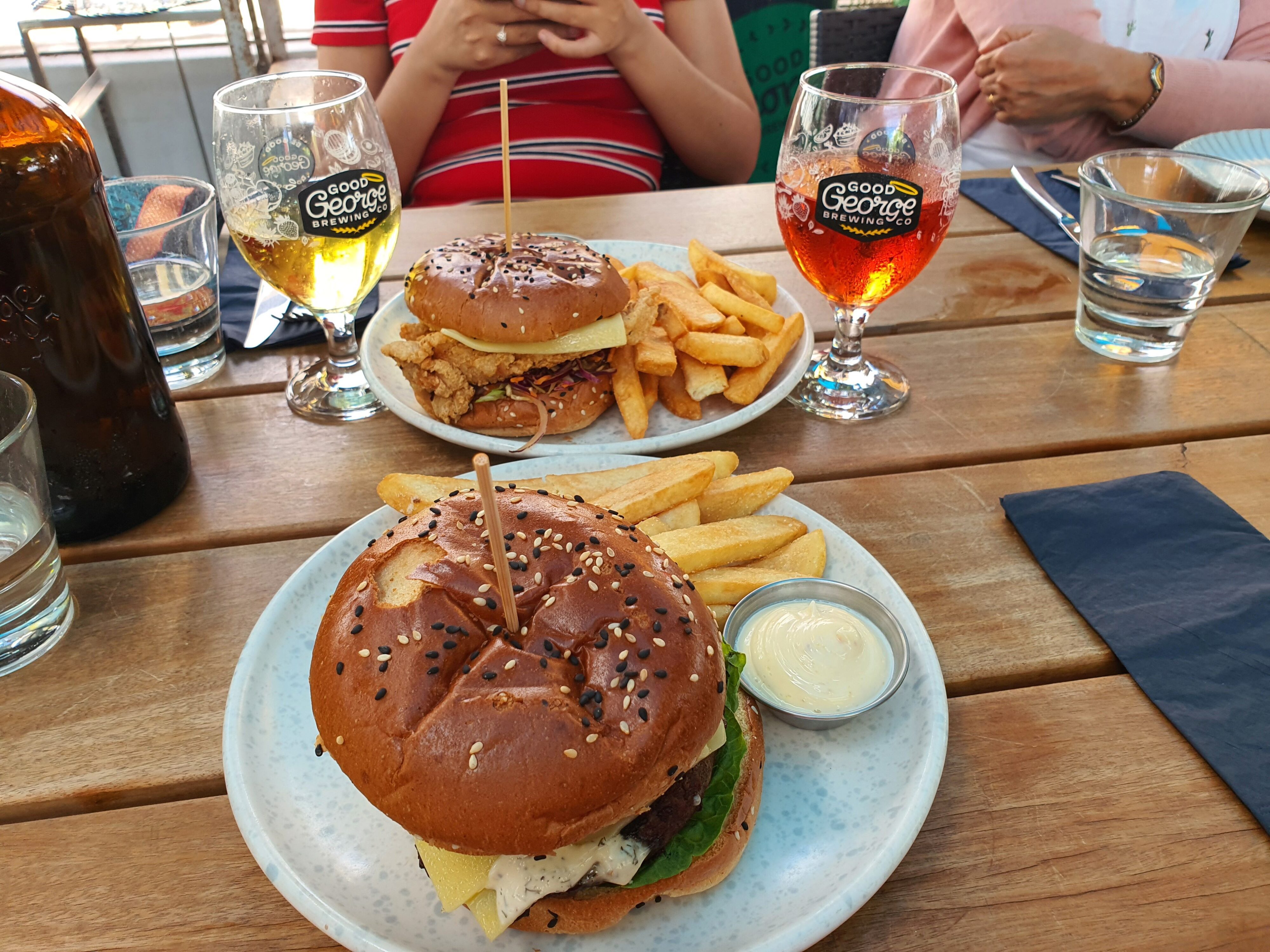 Photo of a lunch meal at Good George Brewing Co, Cambridge, Waikato, New Zealand. Food items pictured are burgers, fries, and two glasses of cider.