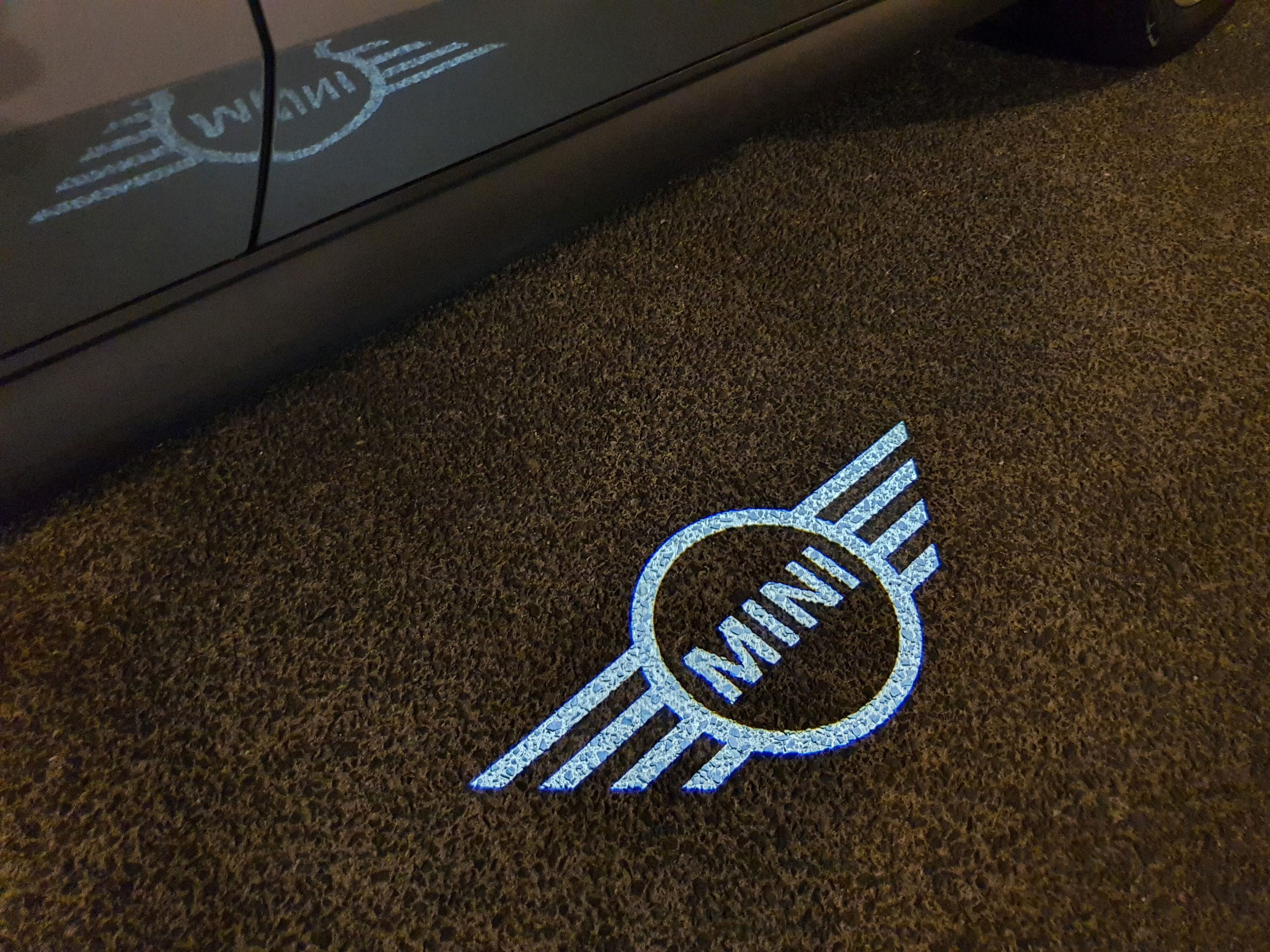 Puddle lighting of the Mini logo on the ground at night.
