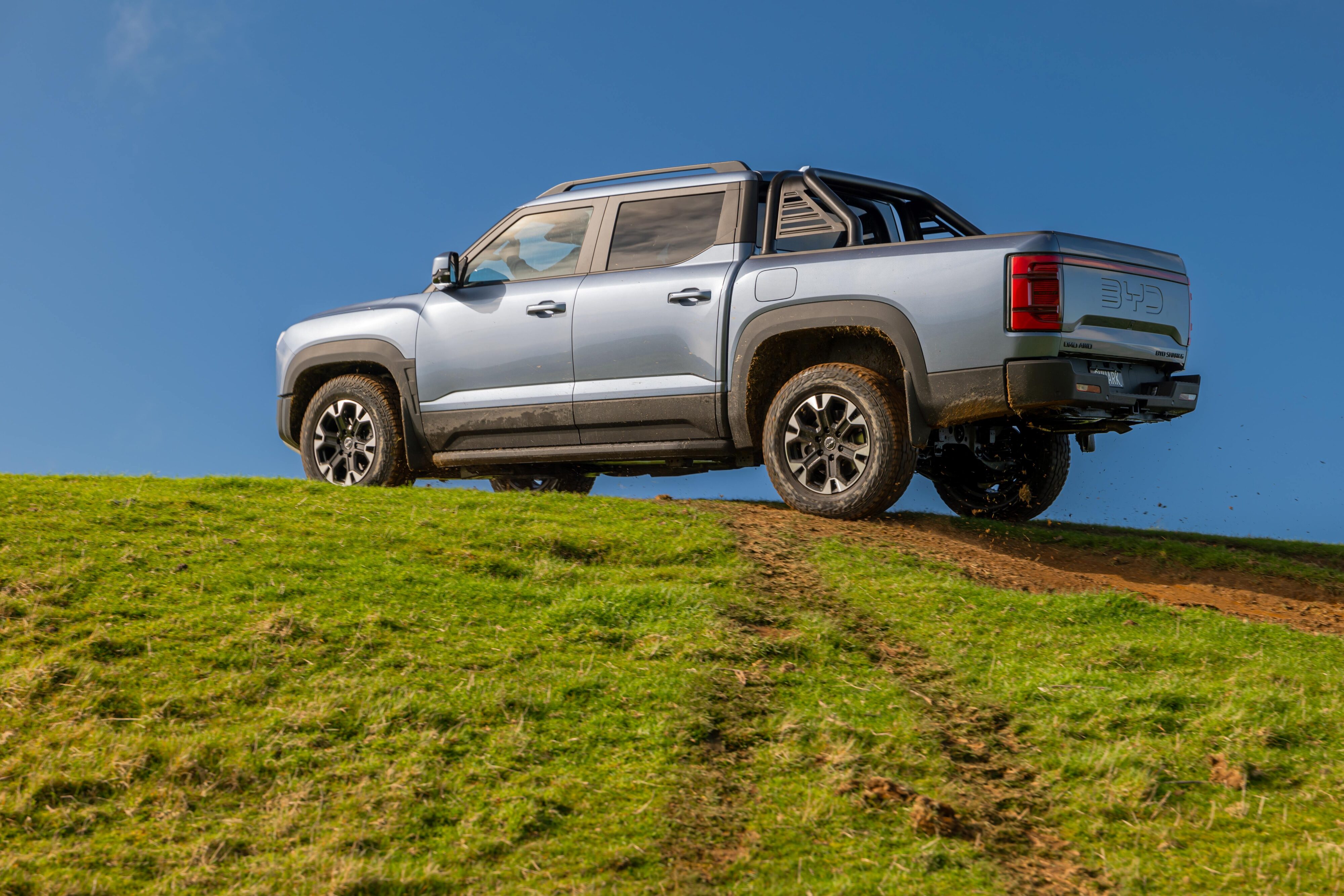 Rear three quarters view of a BYD Shark 6 on a hill.