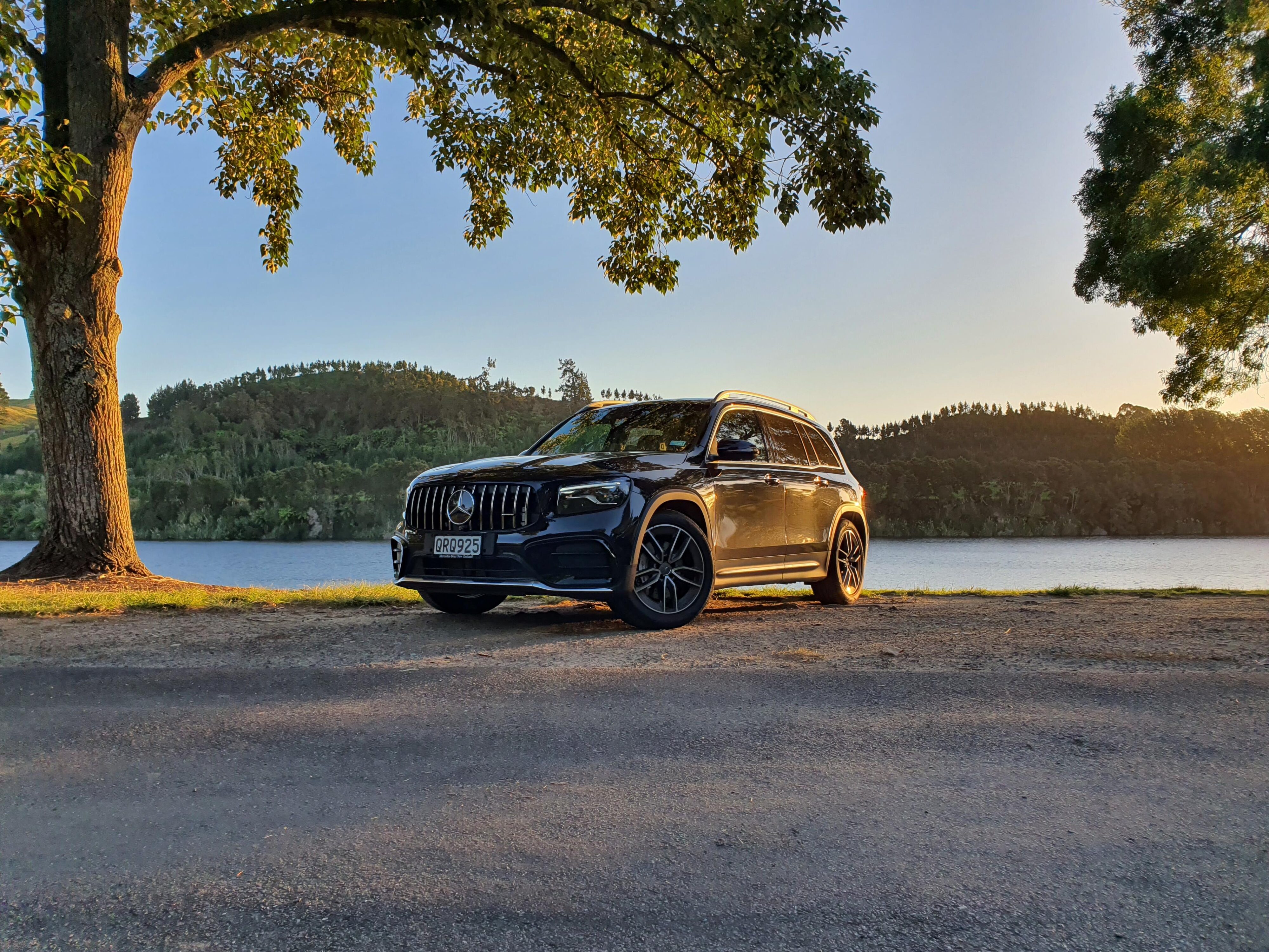 Front three quarters view of a 2024 Mercedes-AMG GLB 35 4MATIC in Black with Lake Karapiro, Cambridge in the background.
