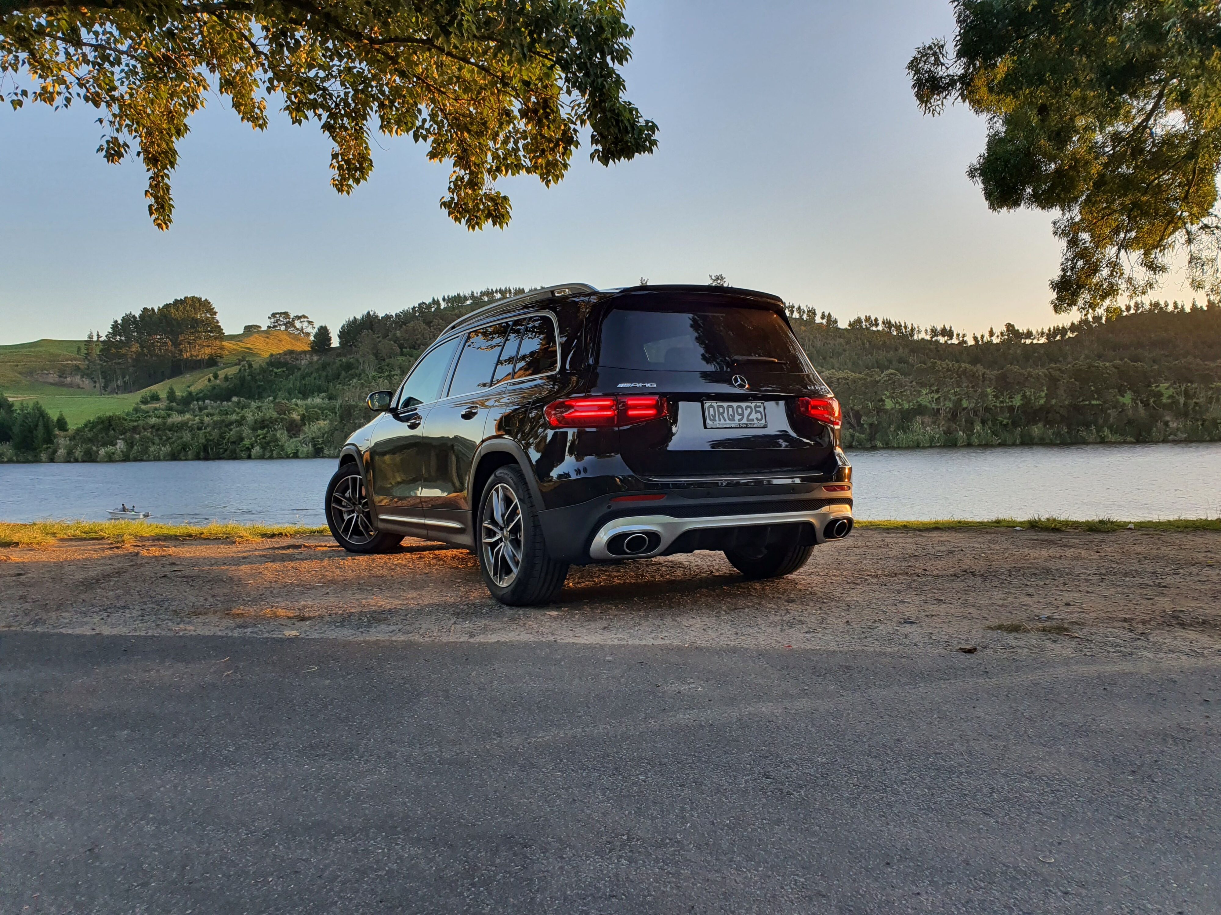Rear three quarters view of a 2024 Mercedes-AMG GLB 35 4MATIC in Black with Lake Karapiro, Cambridge in the background.