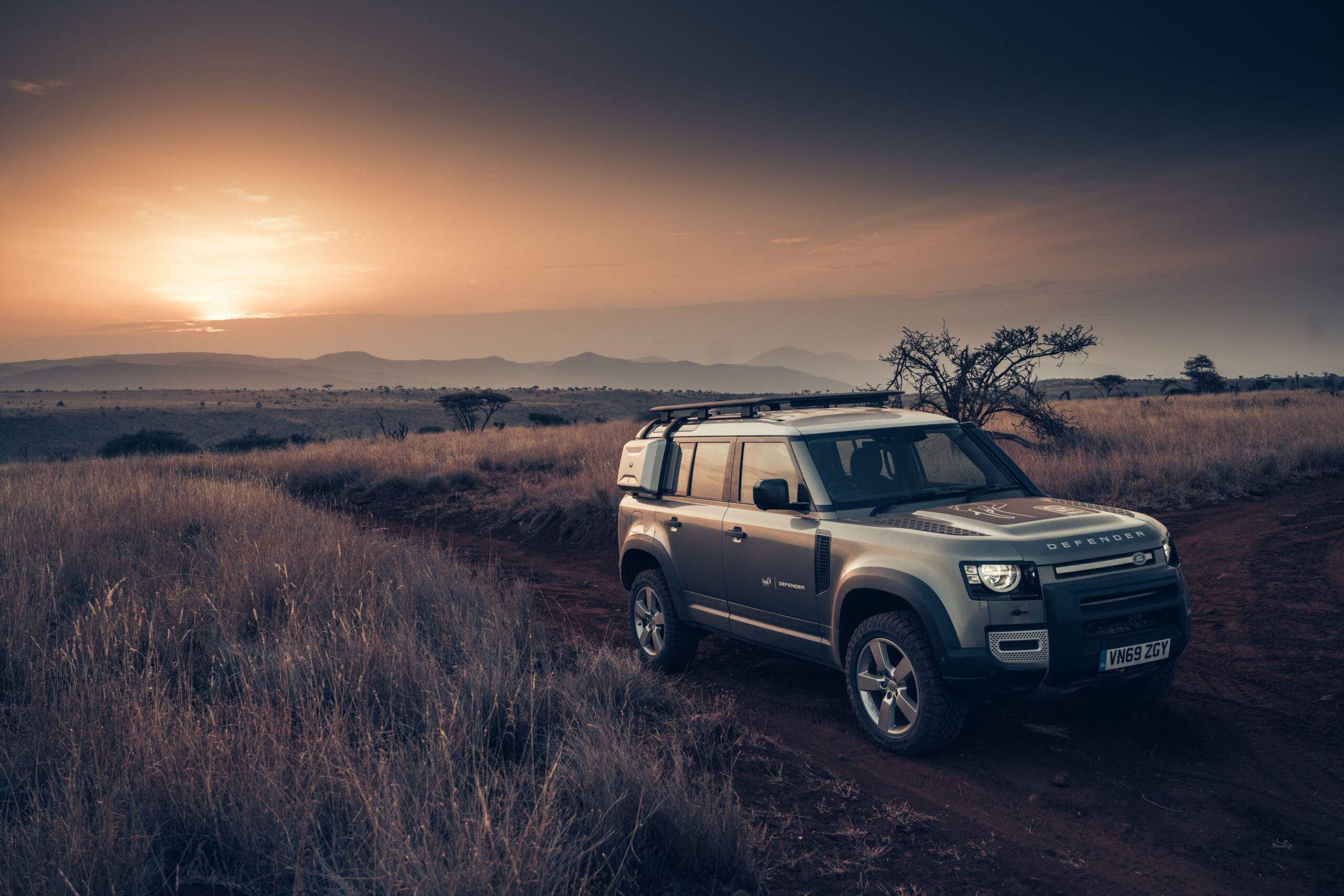 A Land Rover Defender photographed in the African grasslands with the sun set in the background.