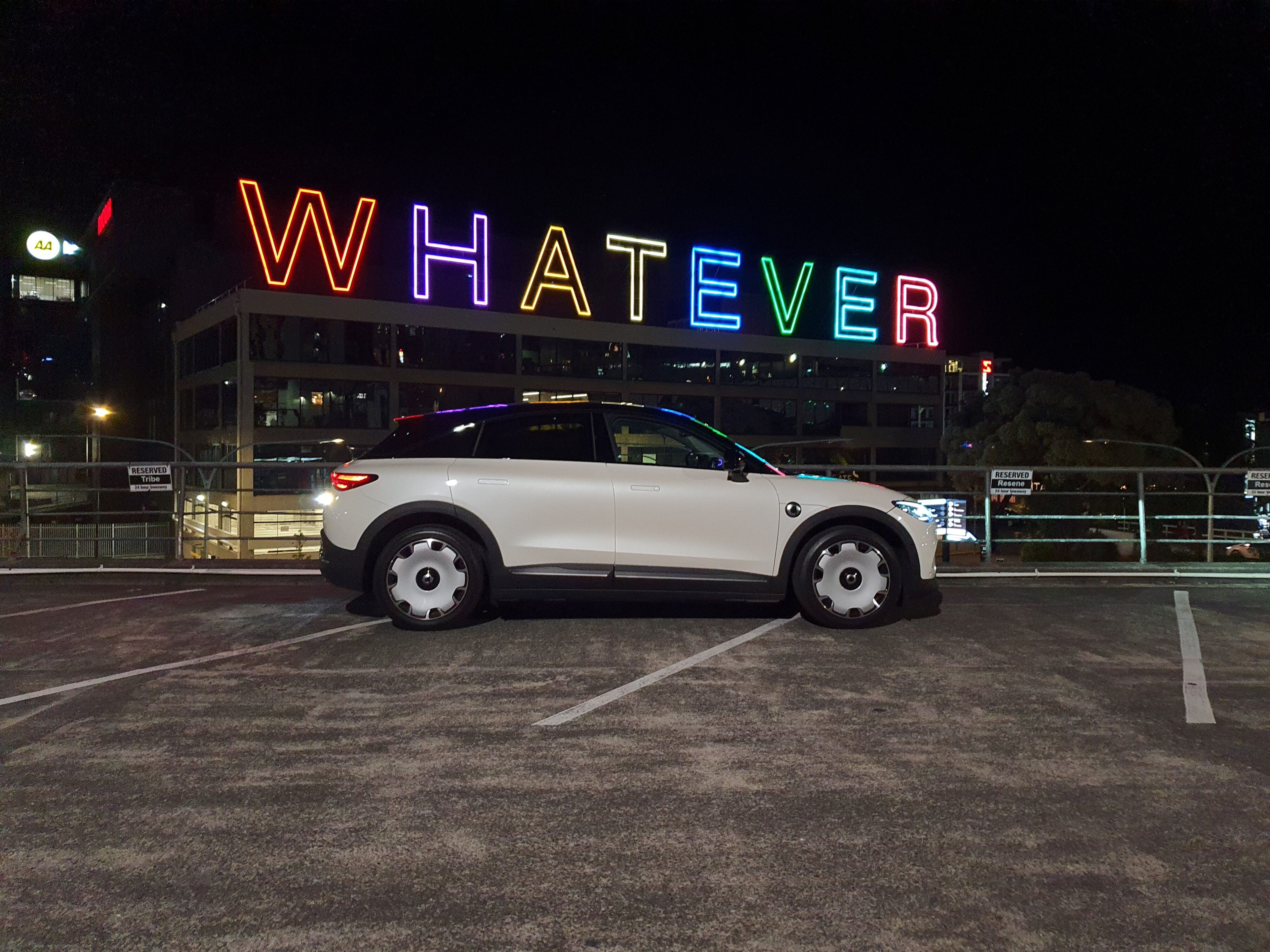 Side on view of a smart #3 Premium in White/Black, photographed at night with the 'Whatever' sign in the background.