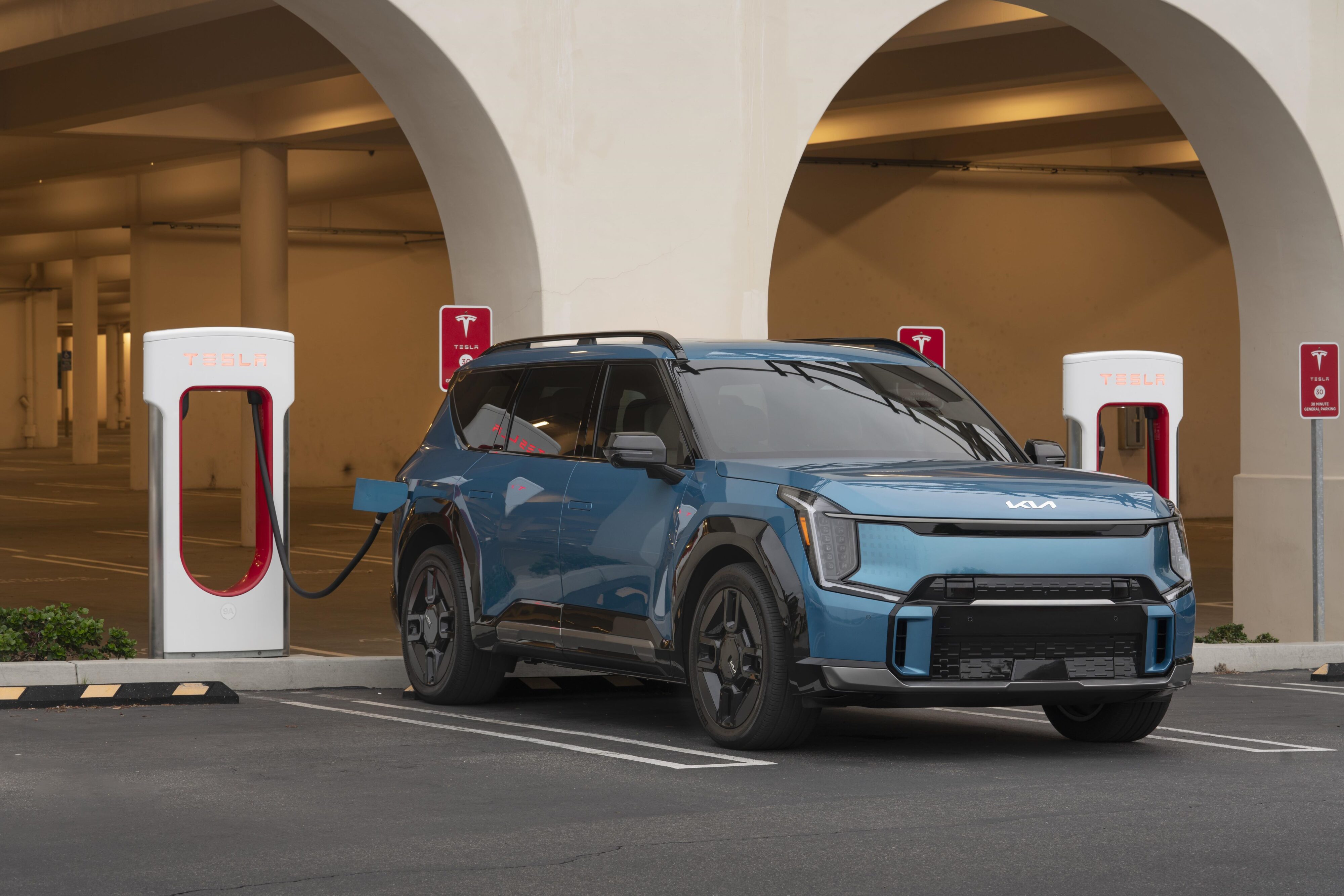 A Kia EV9 plugged in and charging at a Tesla Supercharger.
