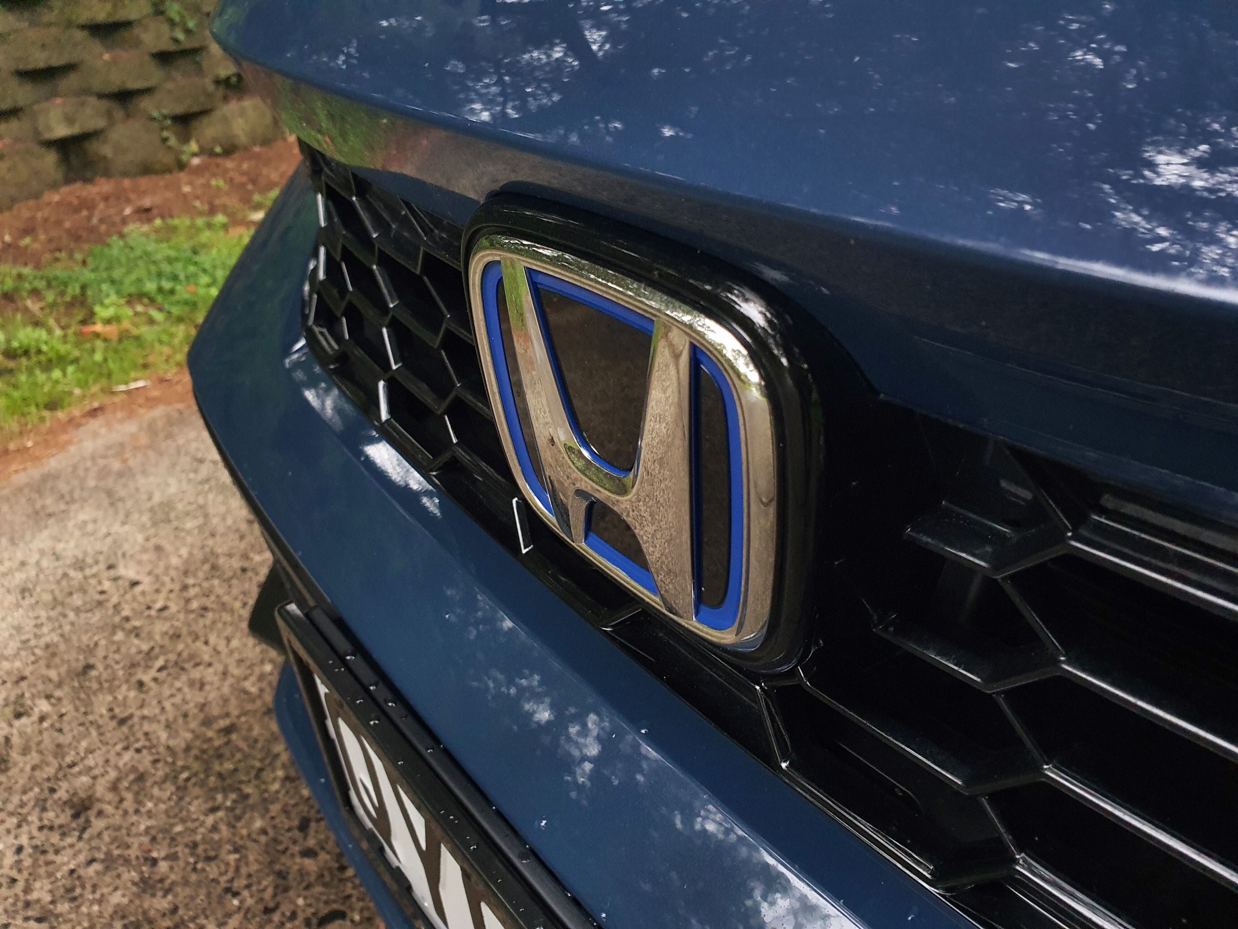 Blue highlighted Honda badge on the front of a 2025 Honda Civic SR e:HEV in Ocean Blue Pearl.