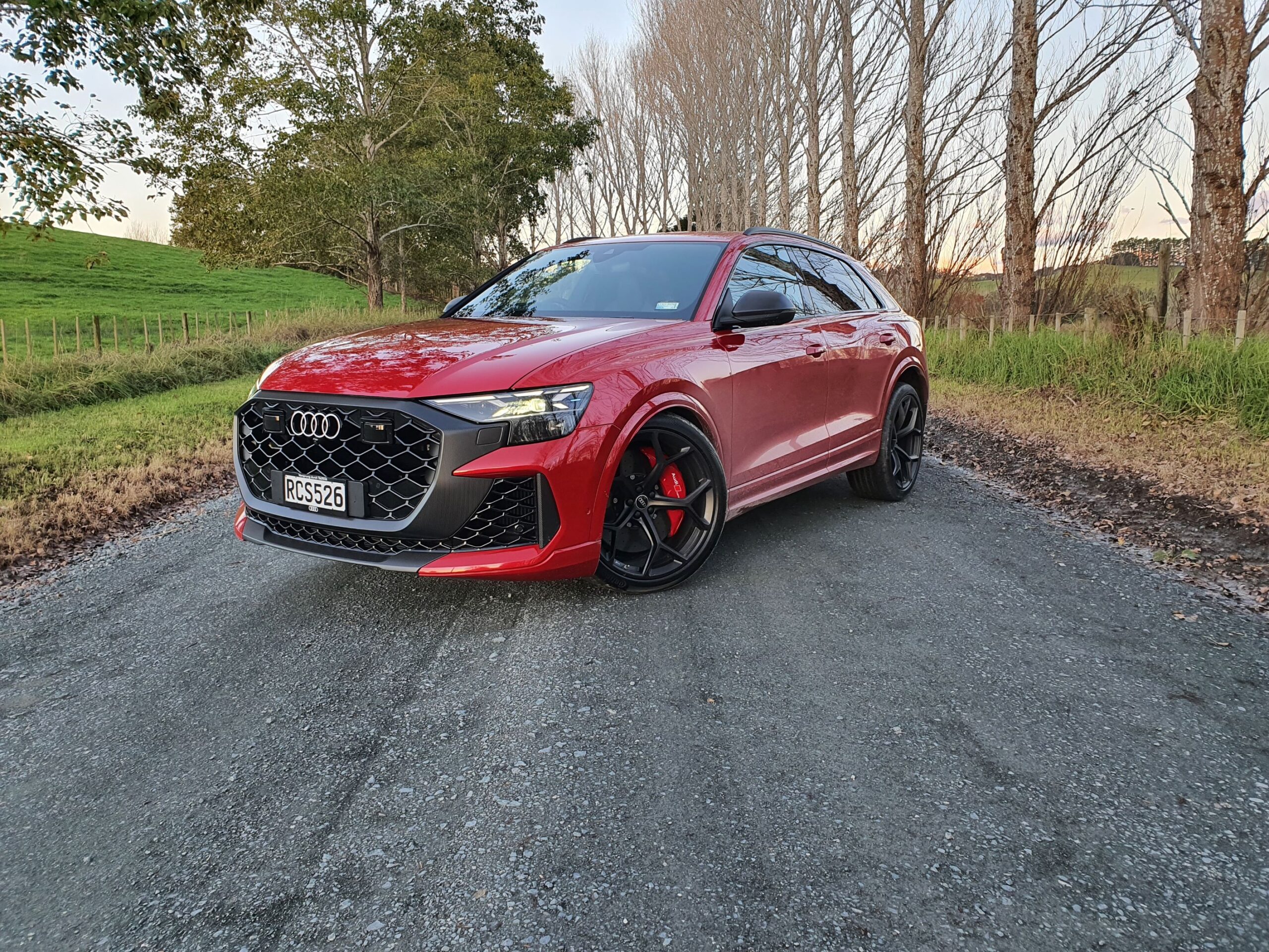 Front three quarters view of a 2025 Audi RS Q8 Performance in Chili Red with bare trees in the background.