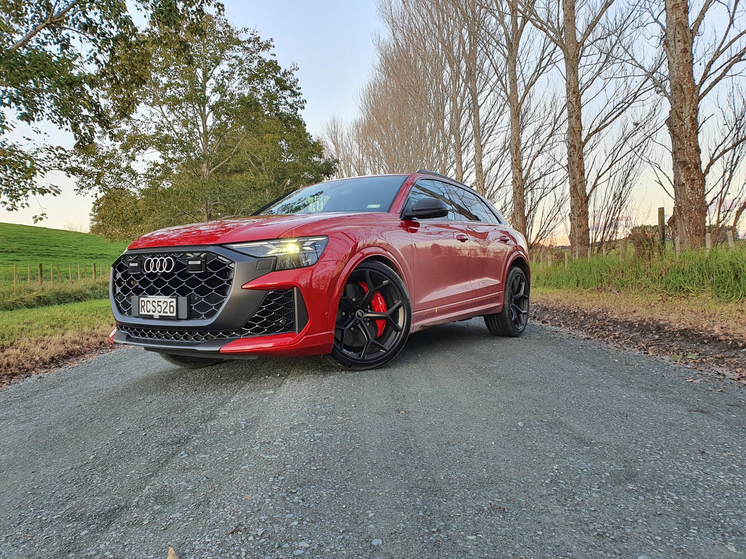 Front three quarters view of a 2025 Audi RS Q8 in Chili Red with bare trees in the background.
