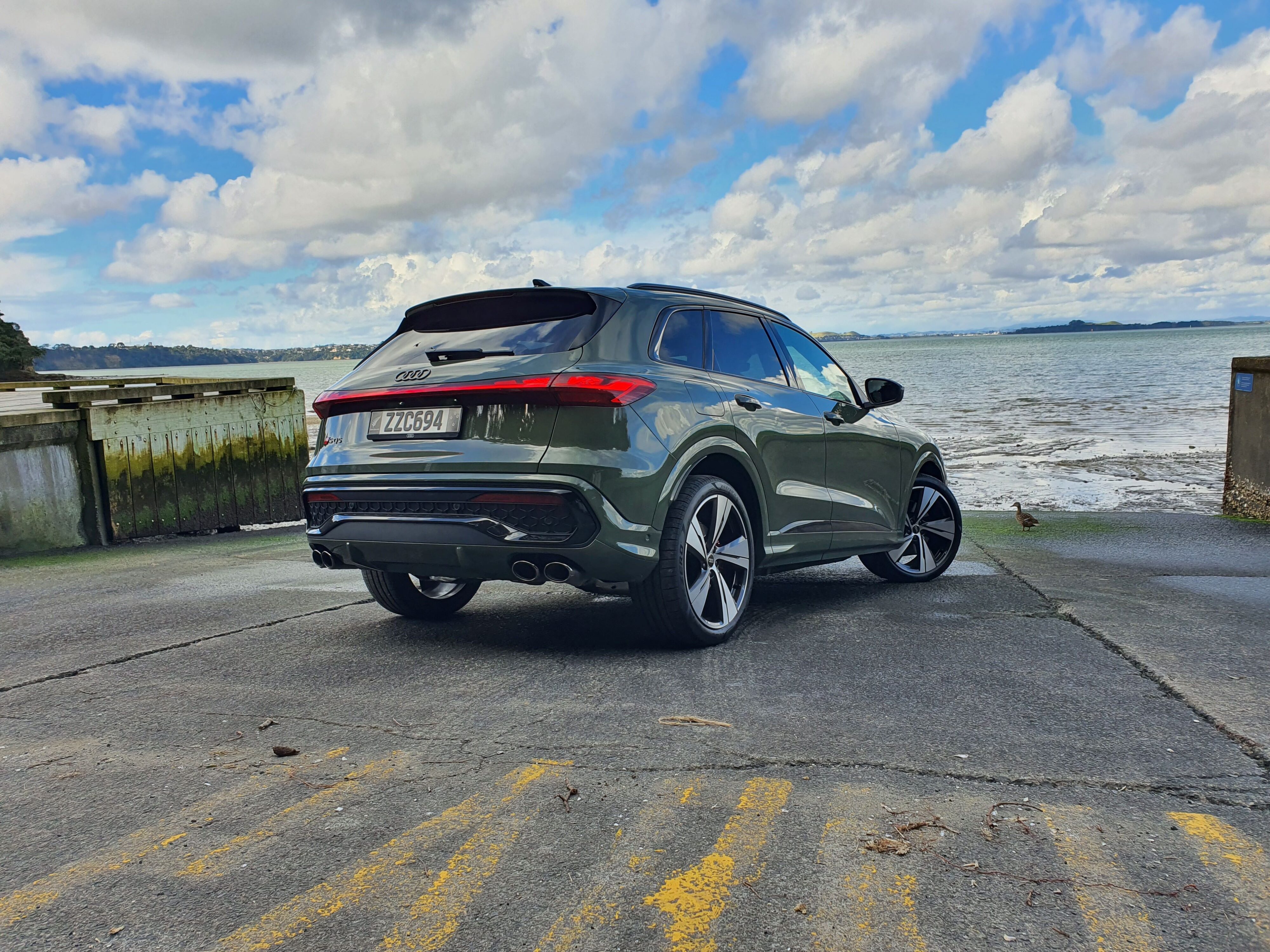 Rear three quarters view of a 2025 Audi SQ5 in District Green with the ocean in the background.